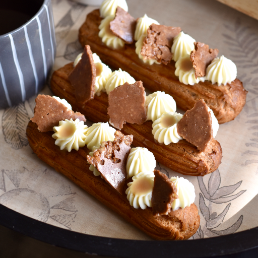 Caramel Latte Eclairs topped with piped cream and chocolate shards